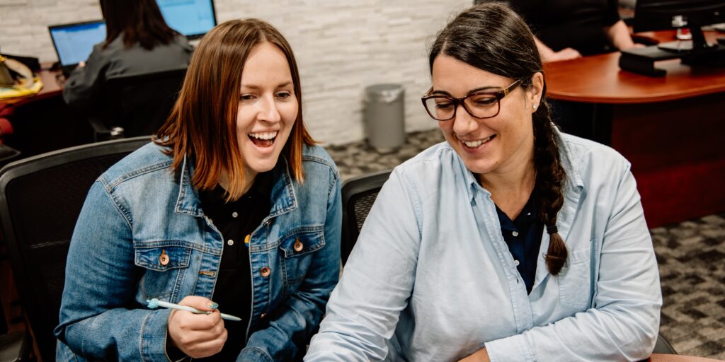 Two women sitting laughing at desk in office