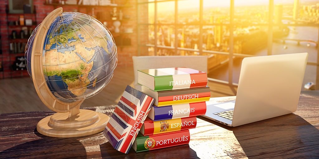 Stack of language dictionaries, globe, and laptop symbolizing Interpro’s support for 128 languages in professional translation services