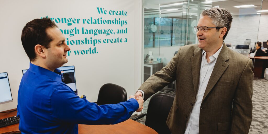 Man, Nicholas Strozza sitting at desk with coworker sitting across from him discussion translation services